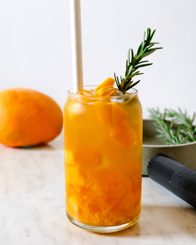 An orange-coloured iced drink with citrus and rosemary